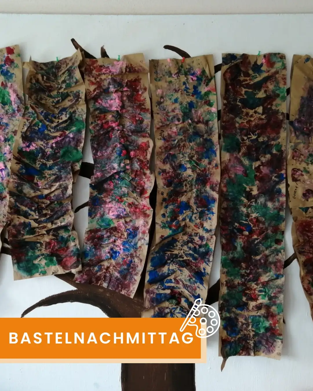 Mehrere längliche, bemalte Papierstreifen, die an einem weißen Hintergrund befestigt sind