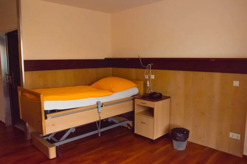 Ein Einzelbett mit oranger Bettdecke und Kissen in einem Zimmer mit Holzwänden und Holzboden neben einem Nachttisch mit Telefon und einem Mülleimer