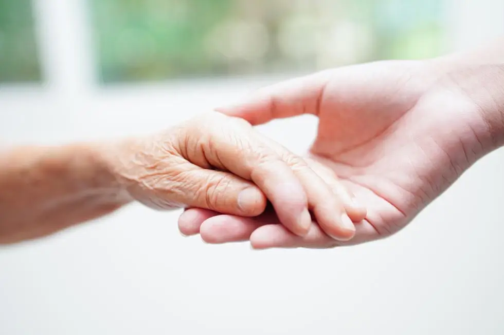 Eine jüngere Hand hält eine ältere Hand in einer unterstützenden Geste